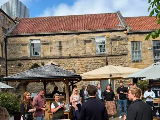 Attendees listening to a welcome talk in the sunny Blackfriars courtyard at a Newcastle First coffee morning.